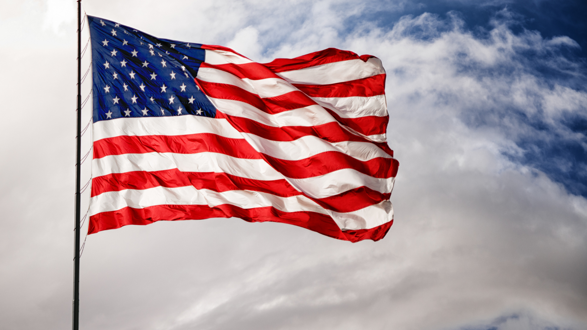 American flag blowing in the wind with a blue sky in the background and clouds